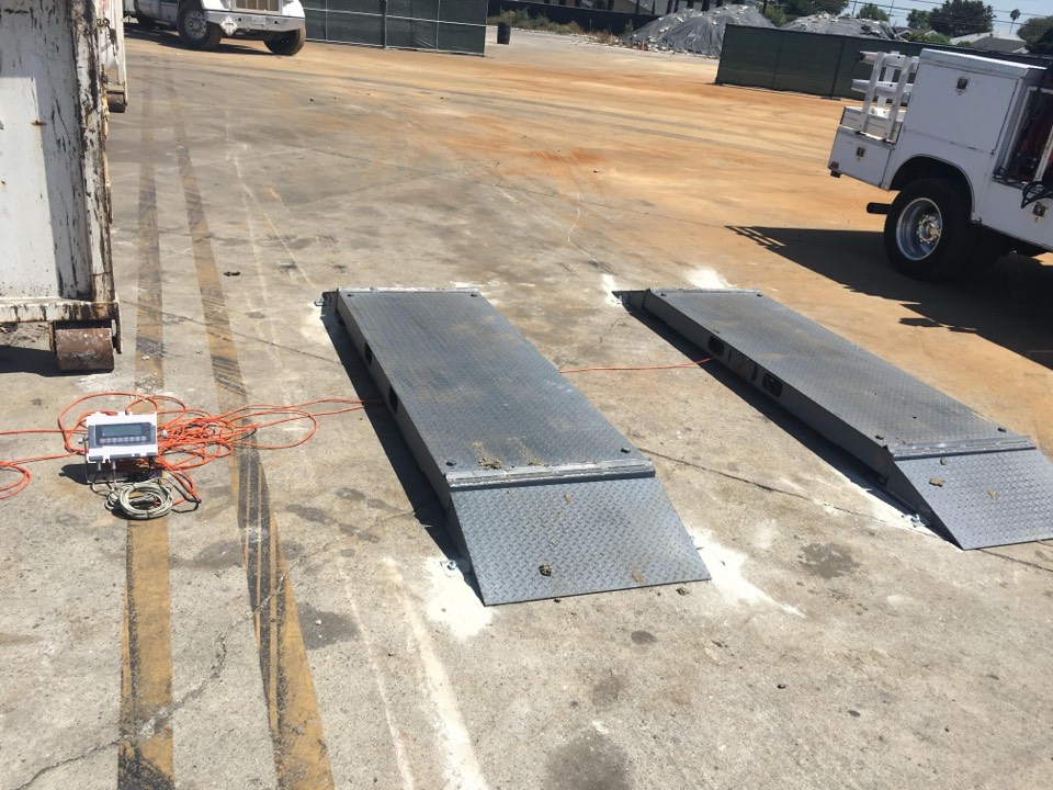 Portable axle-scale weigh pads set up on pavement with a digital weight indicator and a field-service truck, ready for on-site calibration.