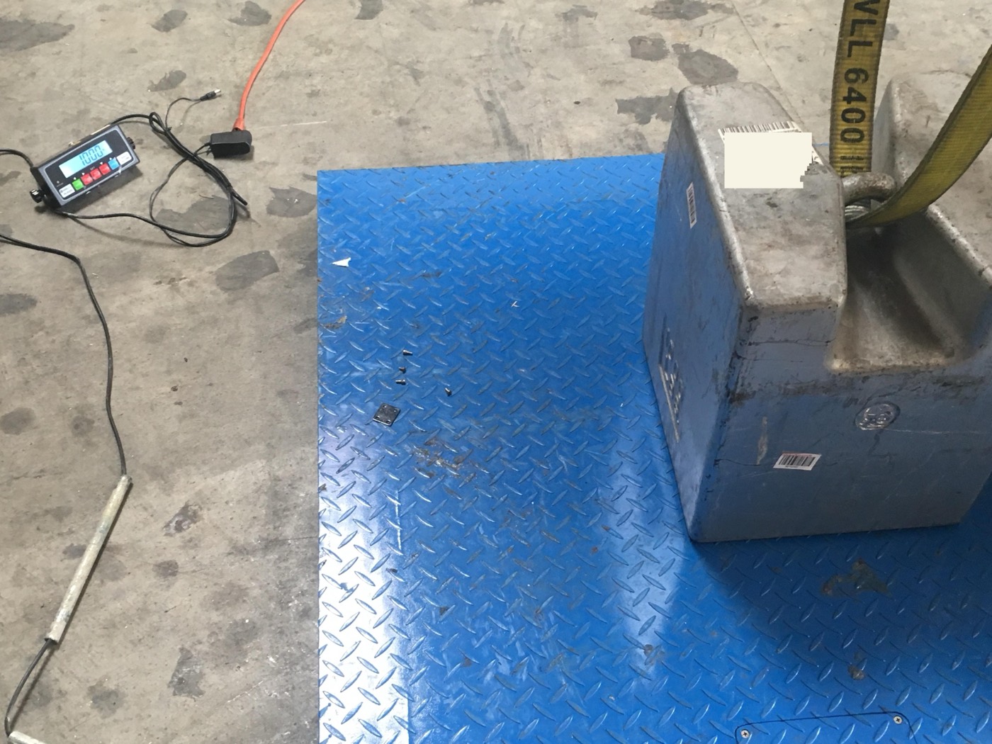 A blue platform floor scale being checked with a stainless steel calibration test weight and a digital indicator.